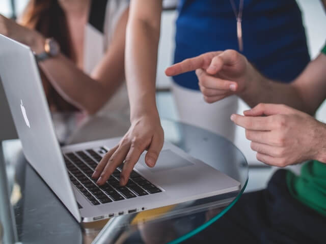 Multiple people are gathered around a table looking at and pointing at a fruit-branded laptop. The subtext to this image is that they are looking at their Energy Report that qualifies them for their BC Energy Efficient Rebate Windows Window Rebate.